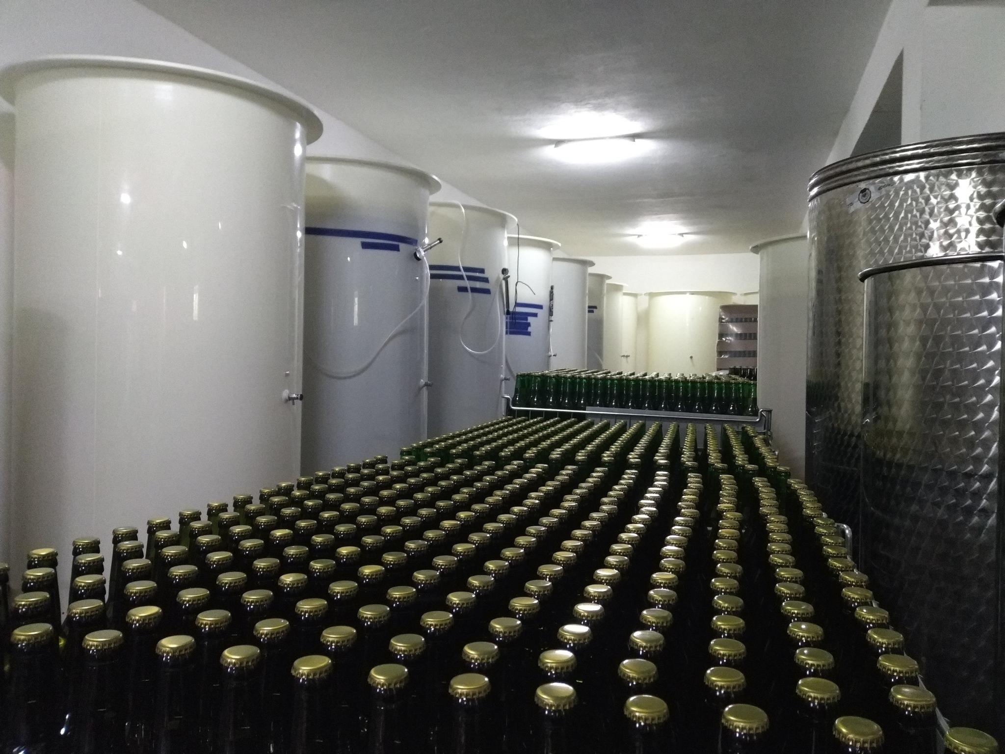 W centrum kadru rżędy butelek, po lewej i prawej stronie tanki fermentacyjne do cydrów.