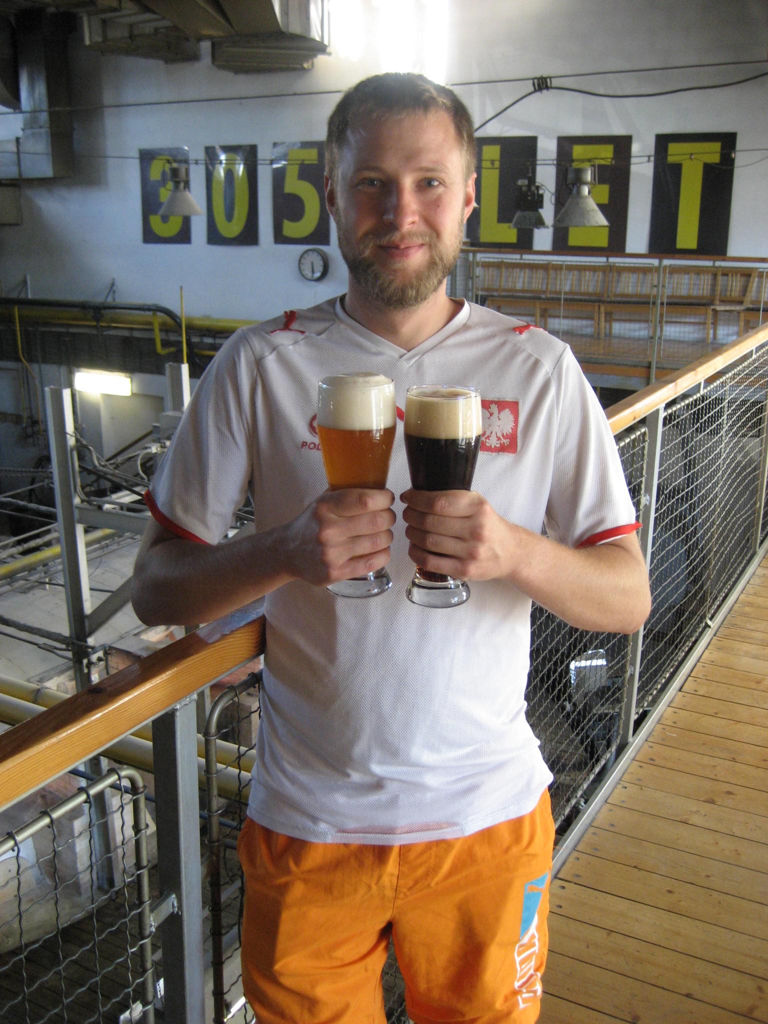 Daniel Duda z Browaru Warmia stojący w browarze trzymający w prawej ręce jasne piwo, w lewej ciemne