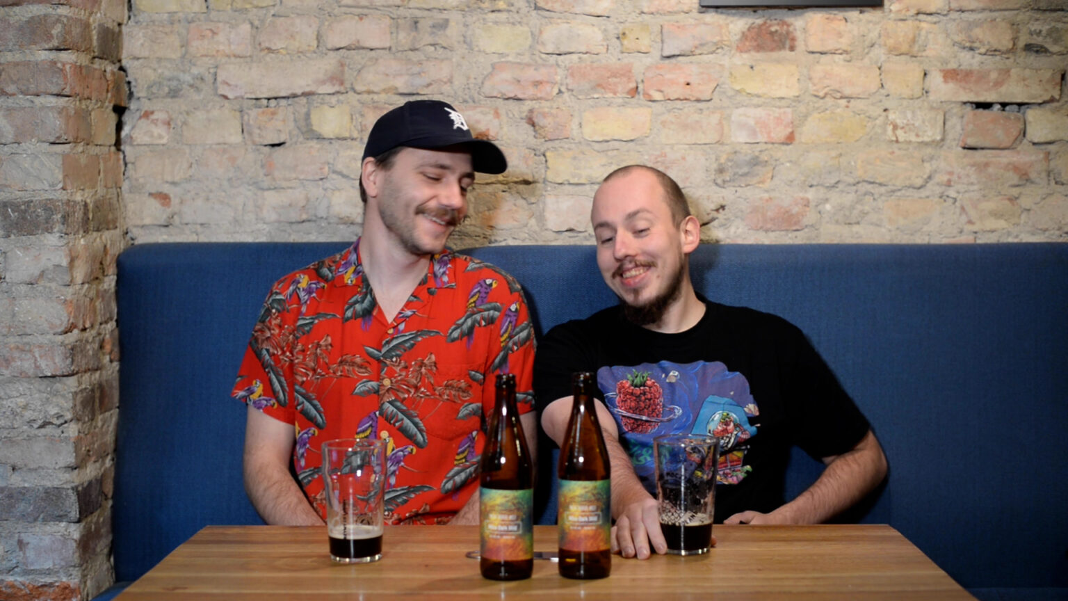Grzegorz Stachurski i Łukasz Szymański siedzą we Wściekłym Chmielu na kanapie i patrzą na stojące na stole butelki piwa Nitro Dark Mild z browaru Moczybroda
